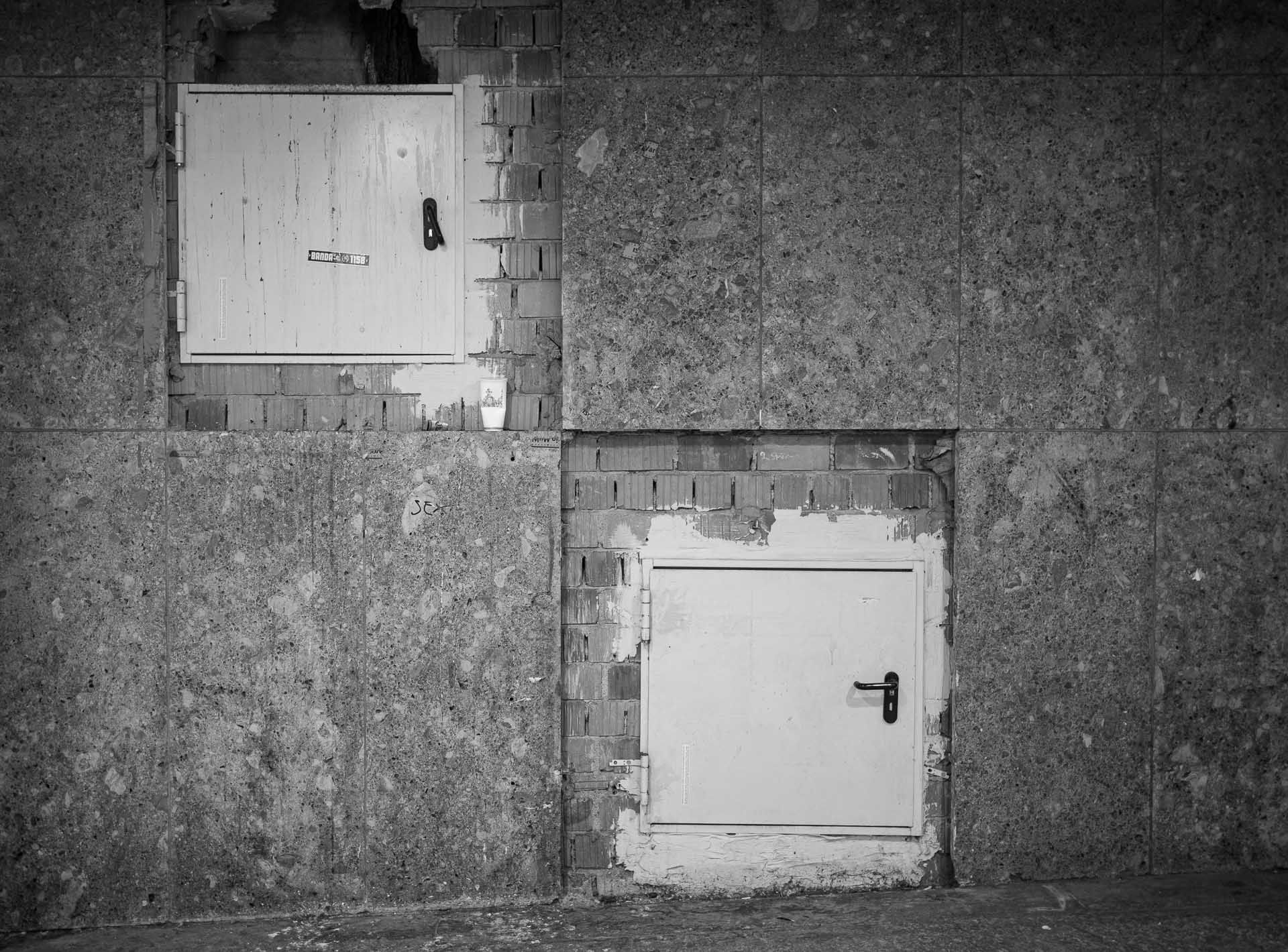 zwei quadratische Türen schräg übereinander in eine Wand hinein