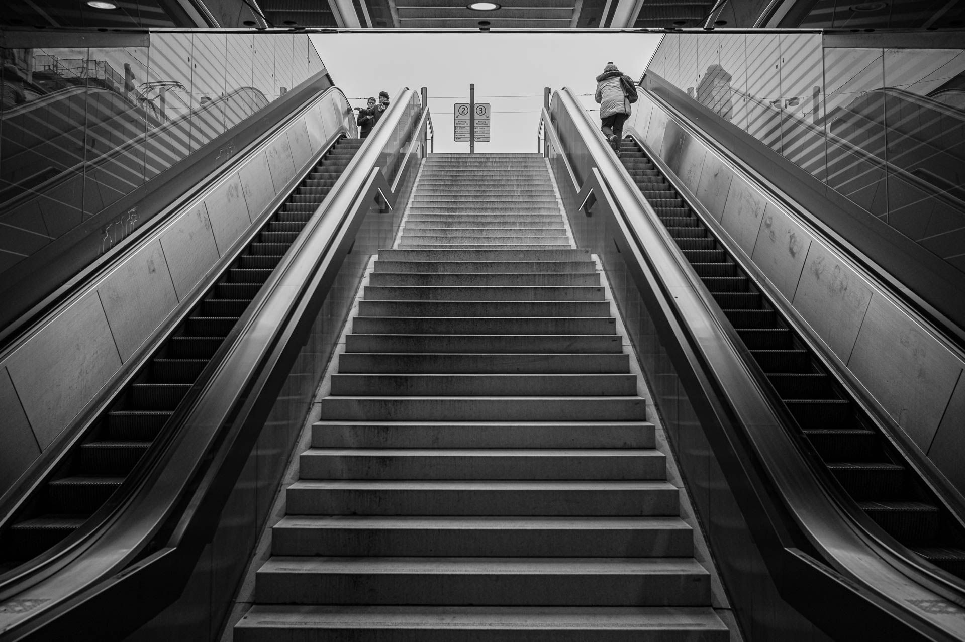 Rolltreppen links und rechts einer Treppe hinauf zur Straßenbahnhaltestelle